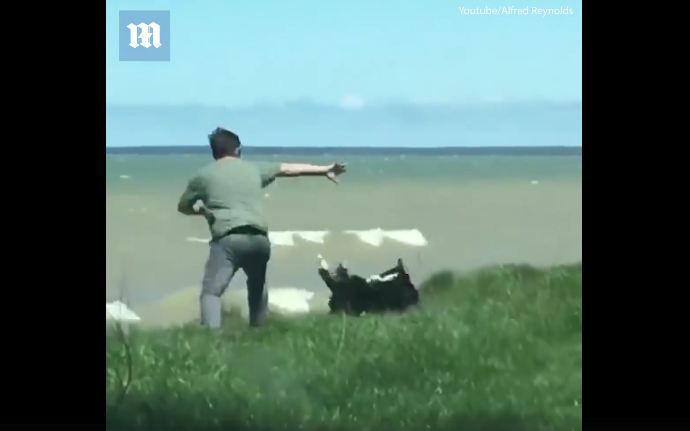 Man’s walking his dog near the water, but the dog doesn’t notice the cliff